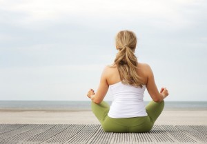 Rear view portrait of  young woman sitting at beach in yoga pose